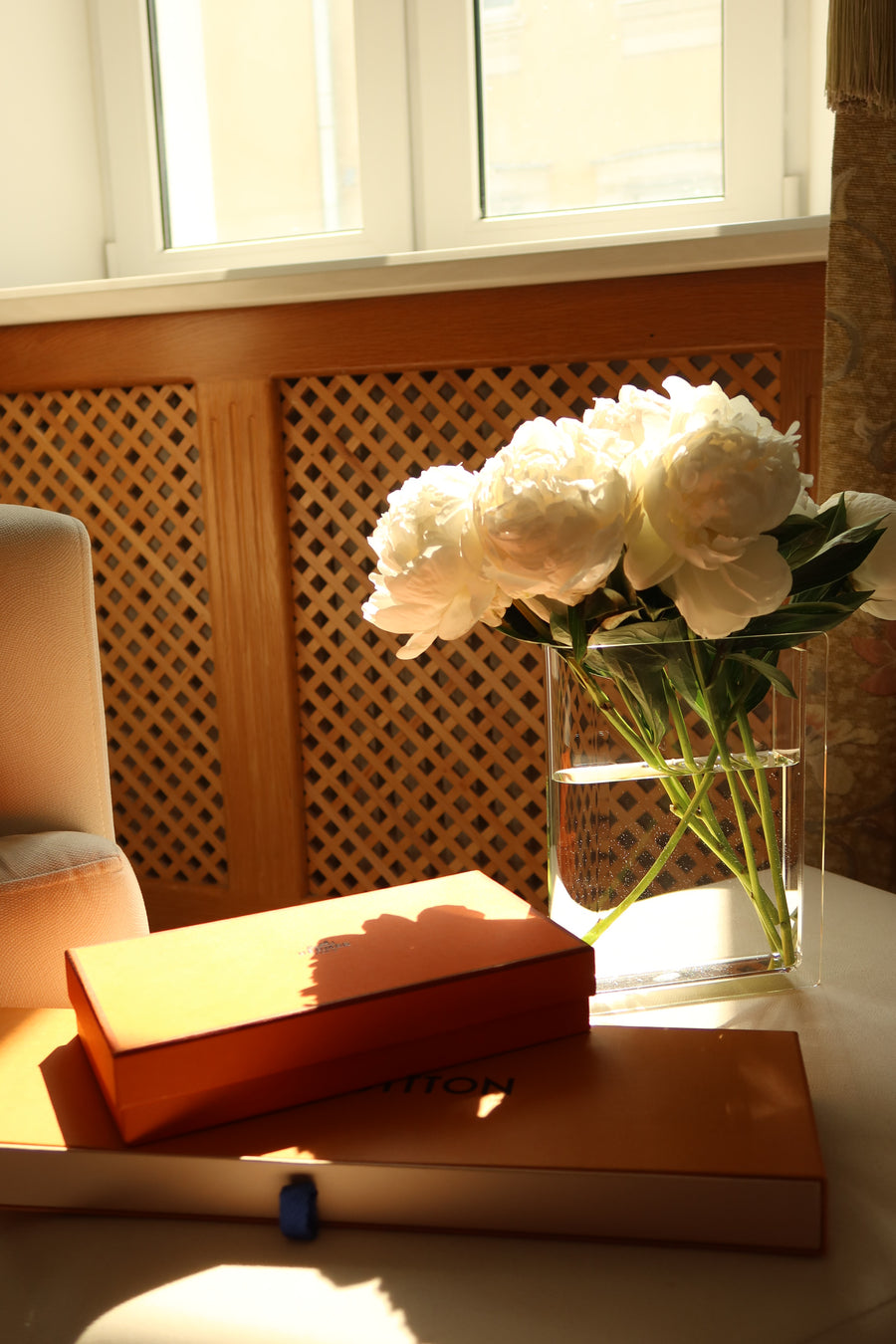 Le Vase Livre, a clear acrylic book vase, holding white peonies on a sunlit side table